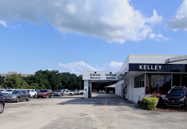 A KELLEY car dealership and service center under a partly cloudy sky, with rows of cars in the lot.