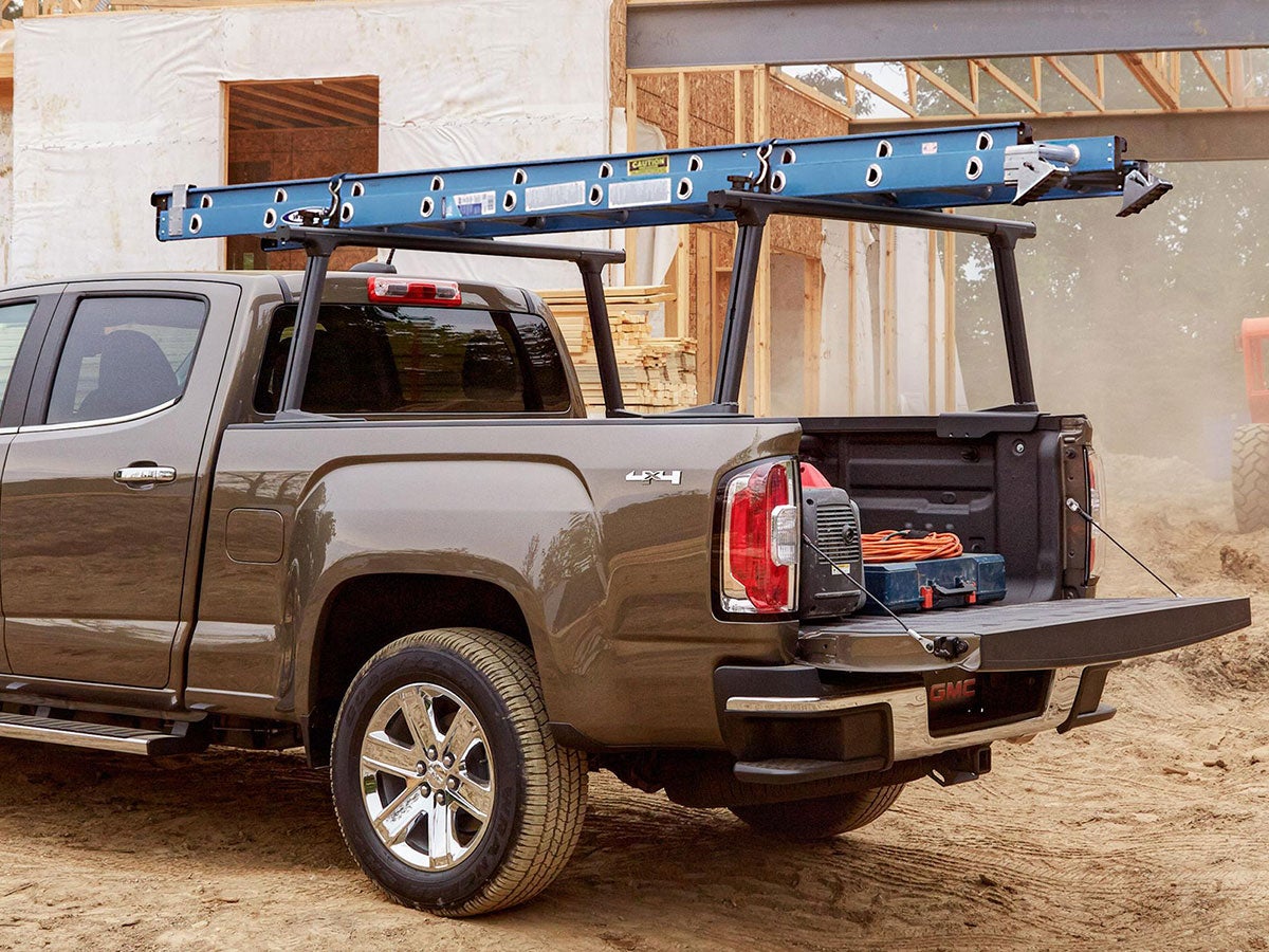 A brown GMC pickup truck with a blue ladder on a rack, parked at a construction site with the tailgate down.