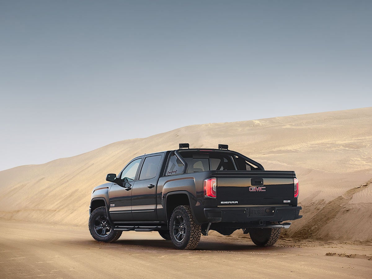 A black 2018 GMC Sierra Black Widow pickup truck from behind, parked on a dirt trail in a desert landscape.