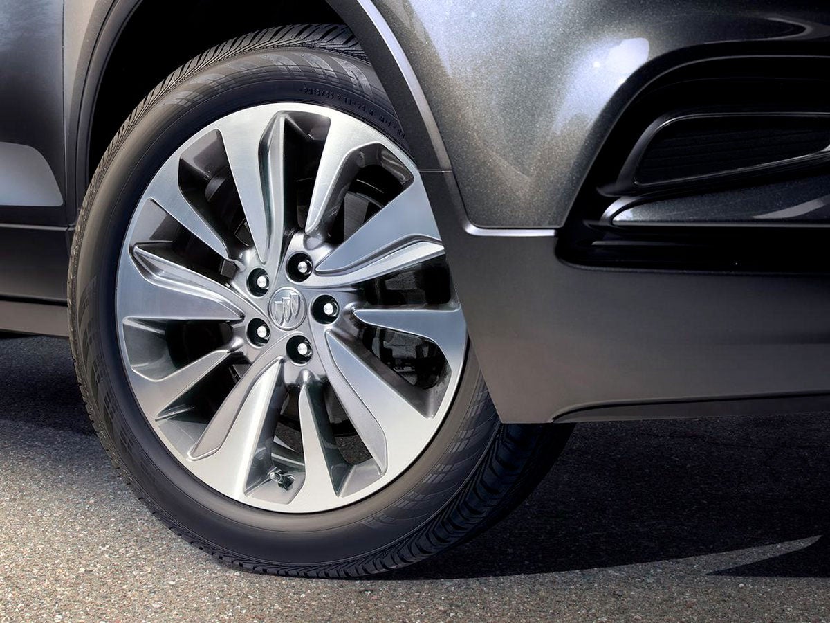 Close-up of a dark gray car's front tire and chrome wheel, with the front bumper visible.
