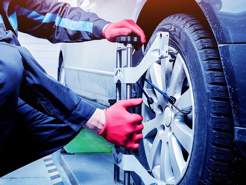 Mechanic in red gloves using tools to perform a wheel alignment on a car tire.